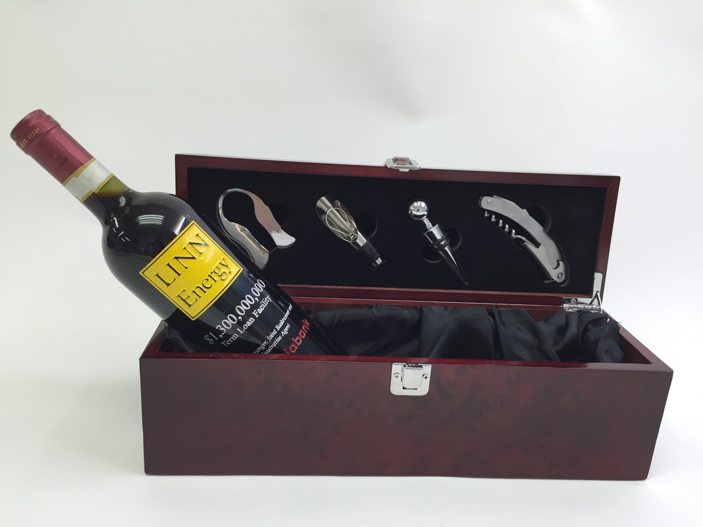 An etched wine bottle marking a term loan facility, resting in an open presentation box beside a four-piece wine tool set.