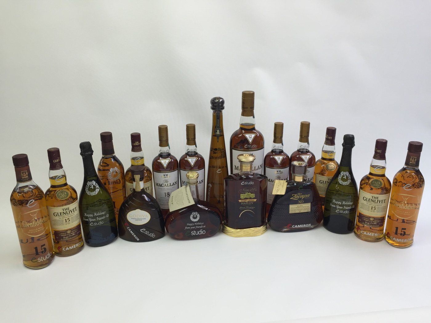 A collection of etched spirits bottles and decanters, including single malt whisky, cognac, rum and liqueur, each carrying the same company mark.
