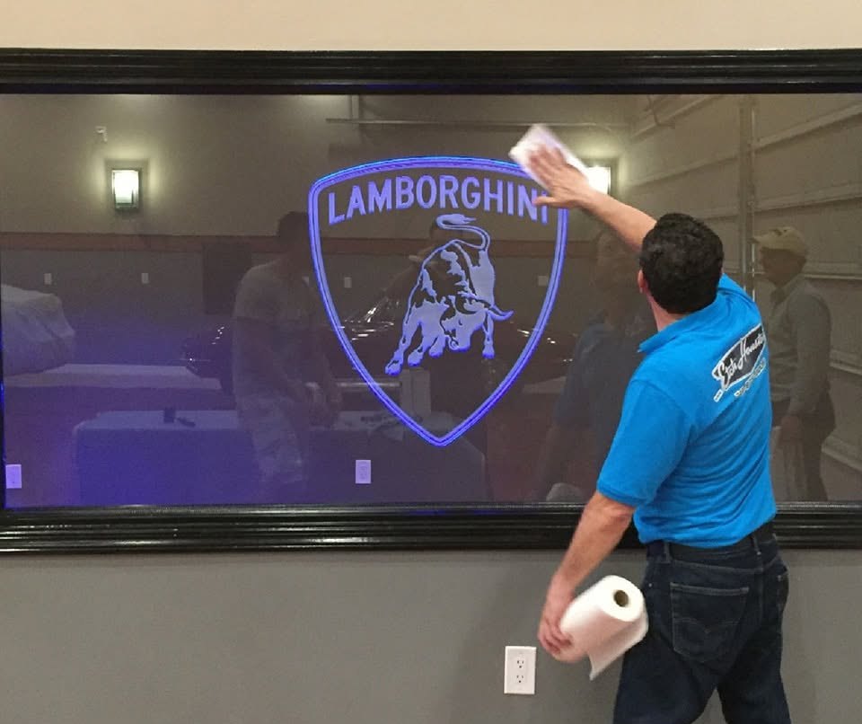 A technician wiping down a large edge-lit glass panel carrying a carved crest that glows violet.