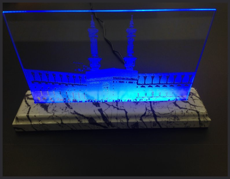 An etched glass panel of a city skyline glowing blue from edge lighting in a stone base.
