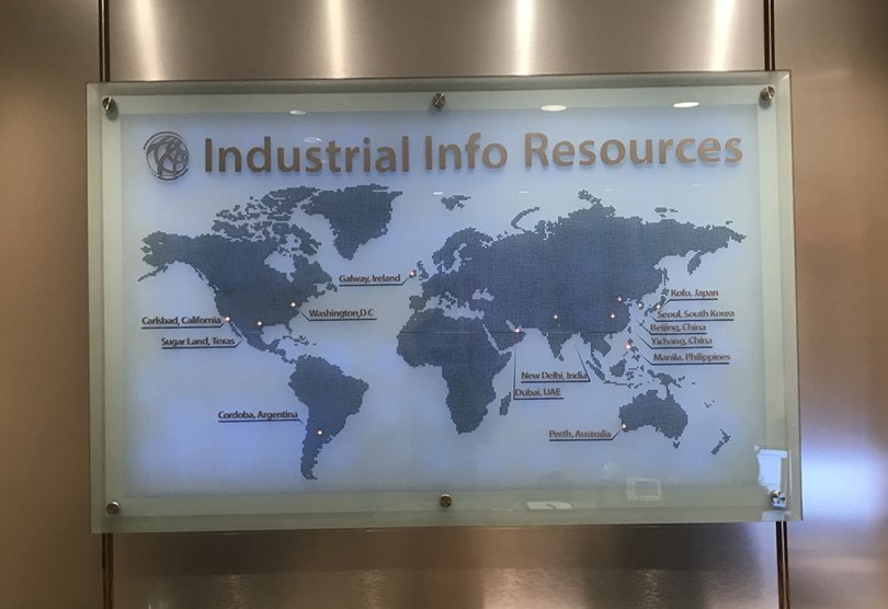 A wide backlit glass panel etched with a world map and location markers, mounted in an office lobby.