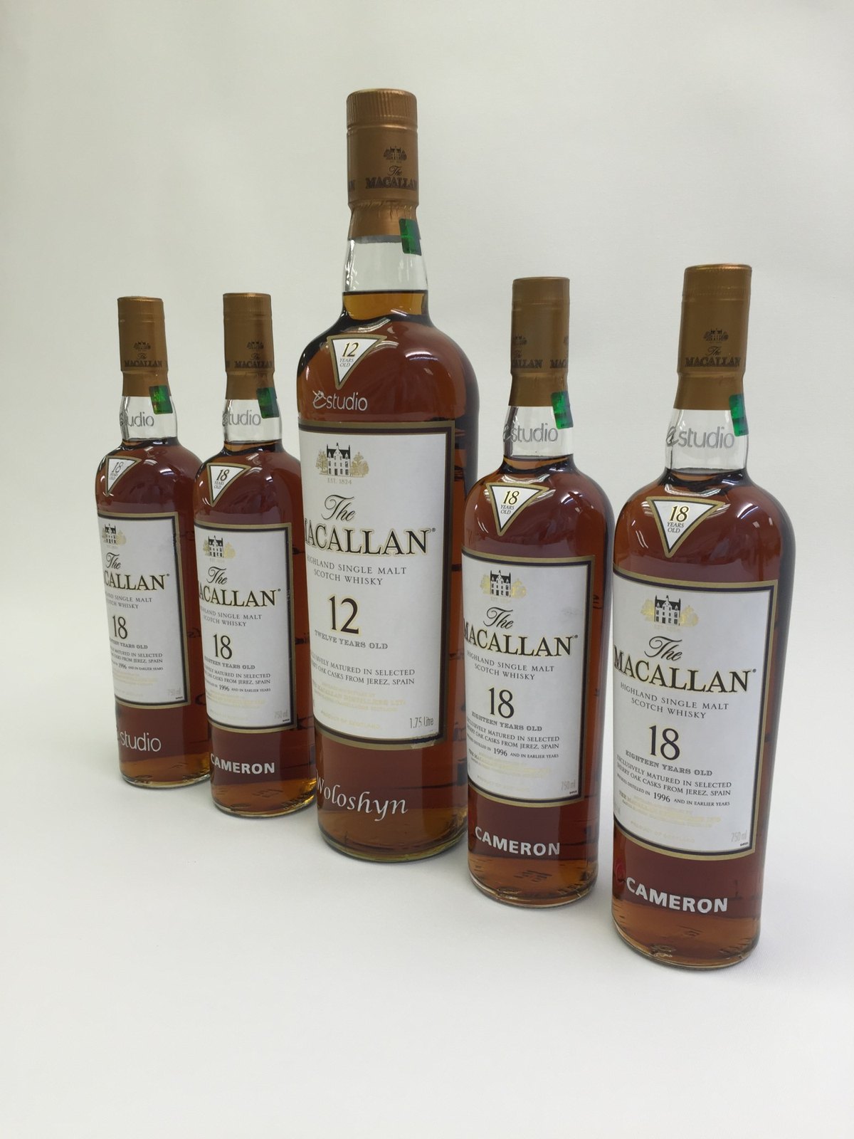Five etched single malt bottles, four standard and one magnum, each carrying a company mark and a different name.