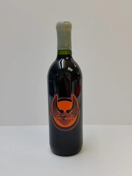 A dark bottle etched with an orange longhorn and star crest, standing on a white surface.