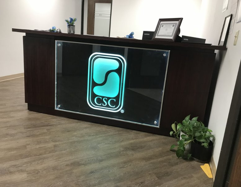 A reception desk fronted with backlit glass carrying an illuminated company mark.