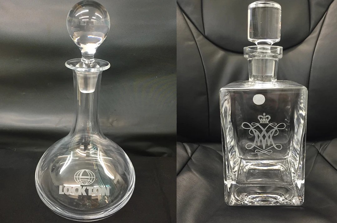 Two etched crystal decanters, one round carrying a company mark and one square carrying a crowned monogram.