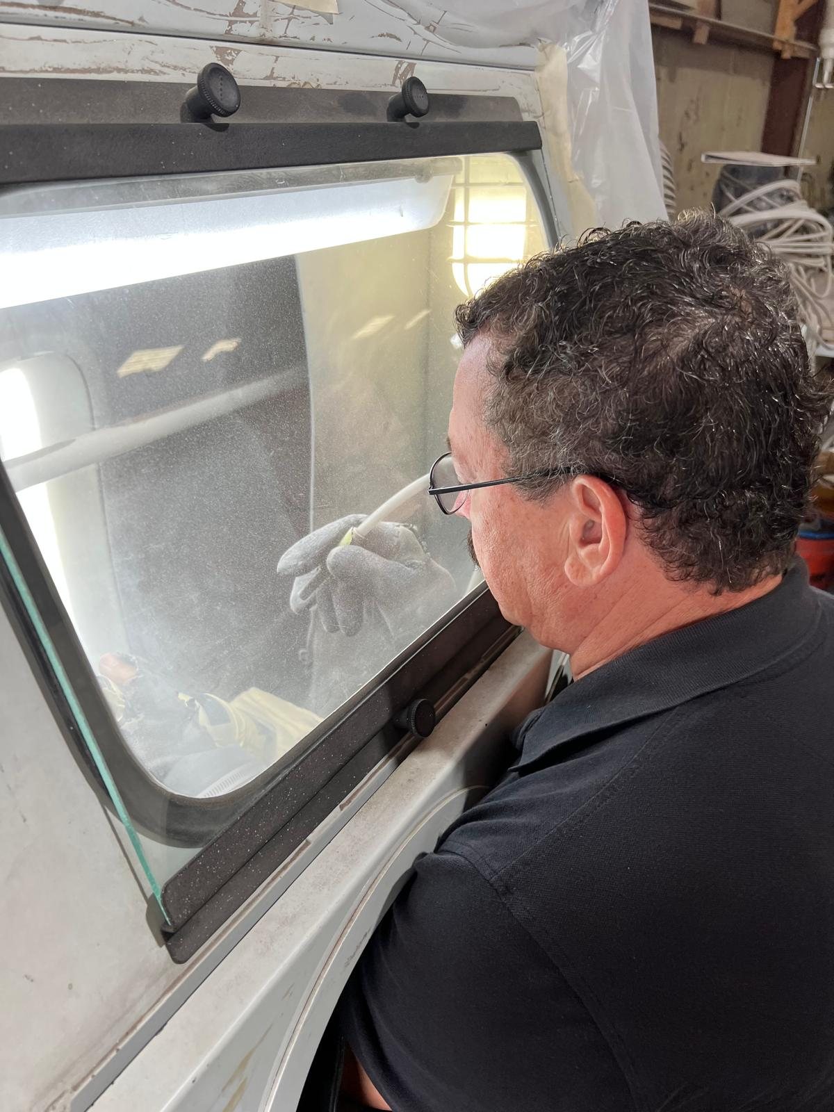 A craftsman at the blast cabinet, hands through the glove ports, sand-carving a panel of glass in the Houston studio.