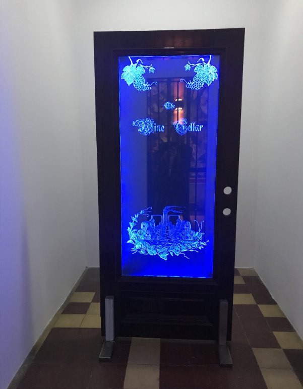 A wine cellar door with a full-height carved glass panel lit blue from inside the cellar.
