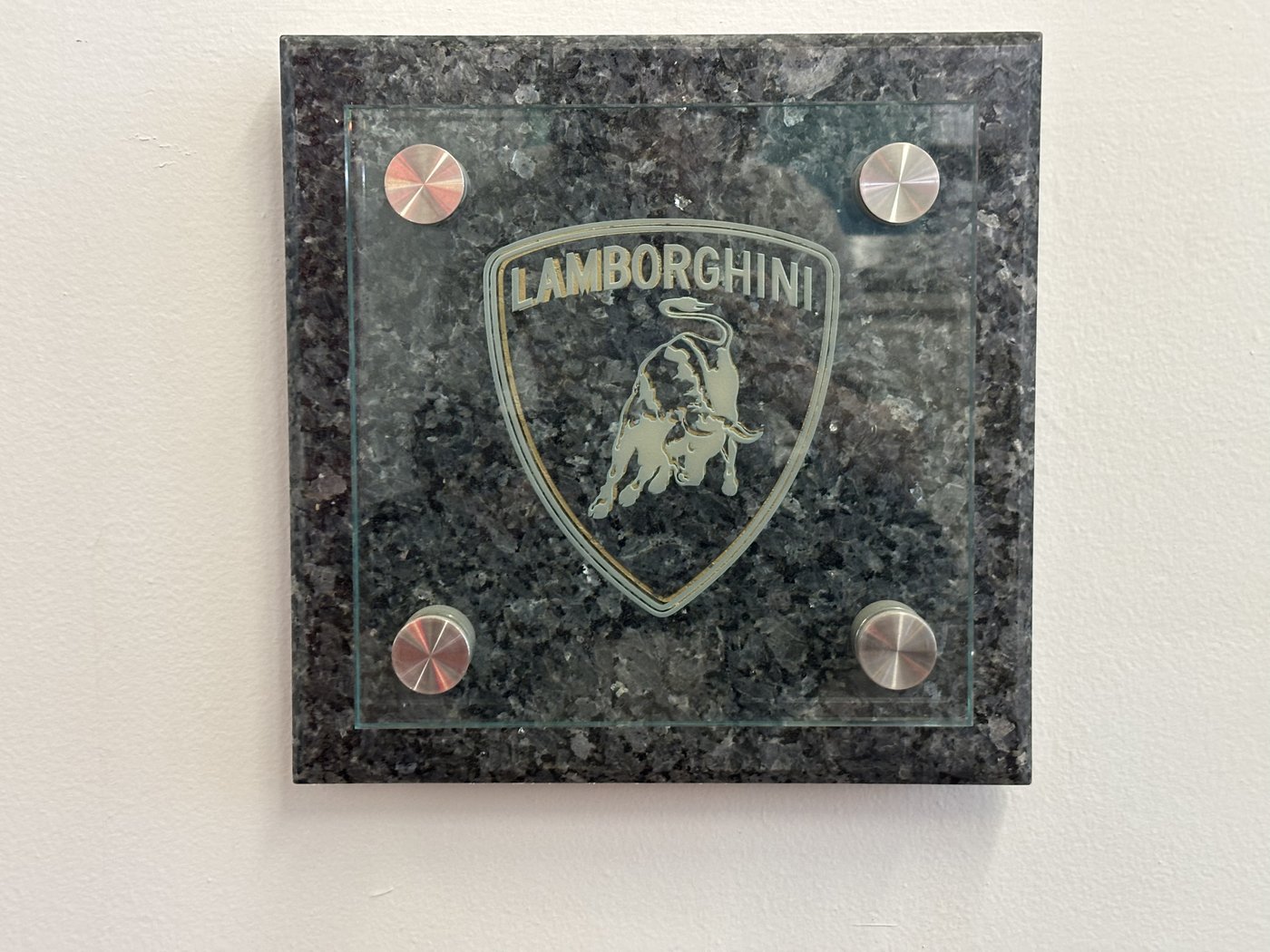 A dark granite plaque engraved with a shield crest, mounted on standoffs against a white wall.