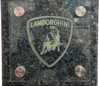 An engraved glass panel carrying a shield crest, mounted on standoffs over a dark granite base.