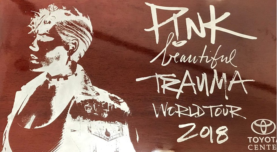 An etched commemorative panel marking a world tour date at an arena, showing a portrait and hand-lettered tour title.