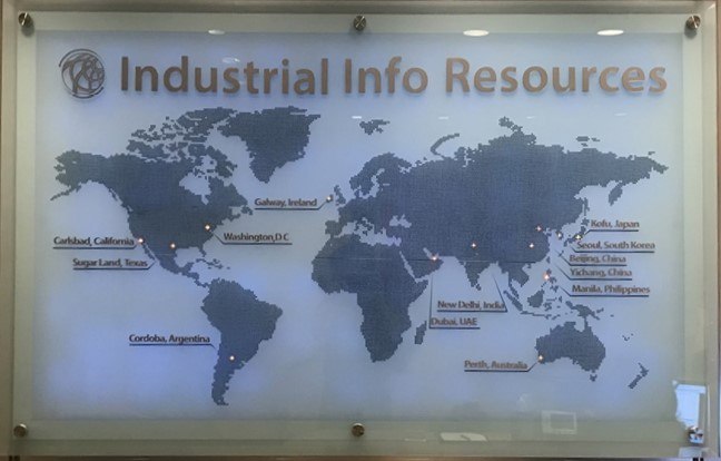 A backlit glass wall panel etched with a world map and location markers in a corporate lobby.