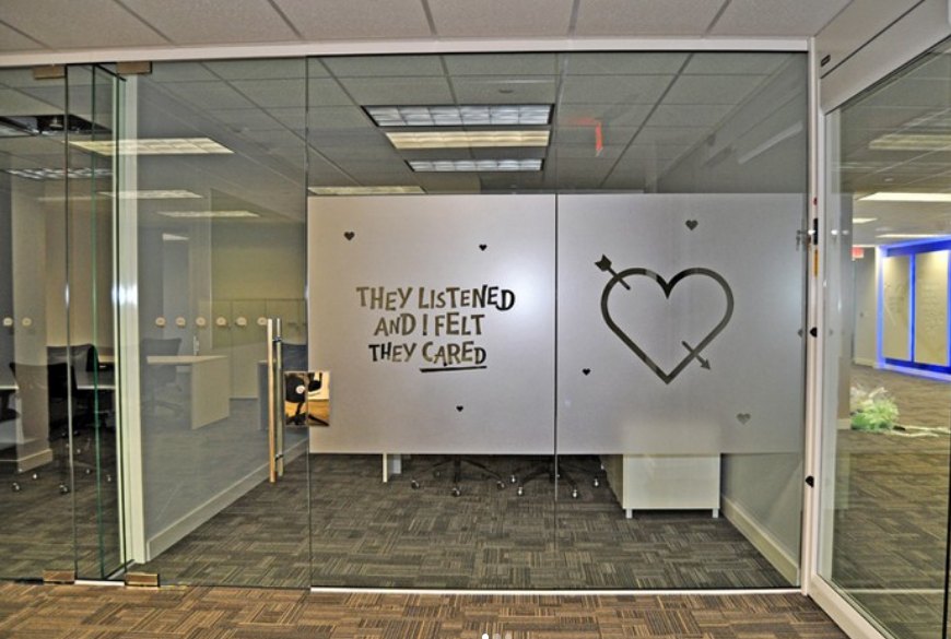 A glass-walled office meeting room with frosted film panels carrying a hand-lettered quote and a large heart graphic.