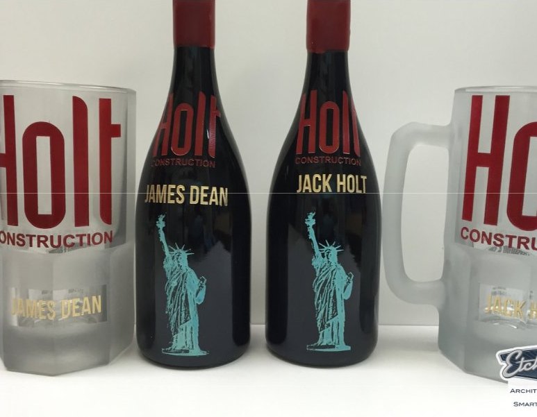Etched bottles and matching frosted glass mugs branded with a construction company mark, each bottle personalised with a different name.