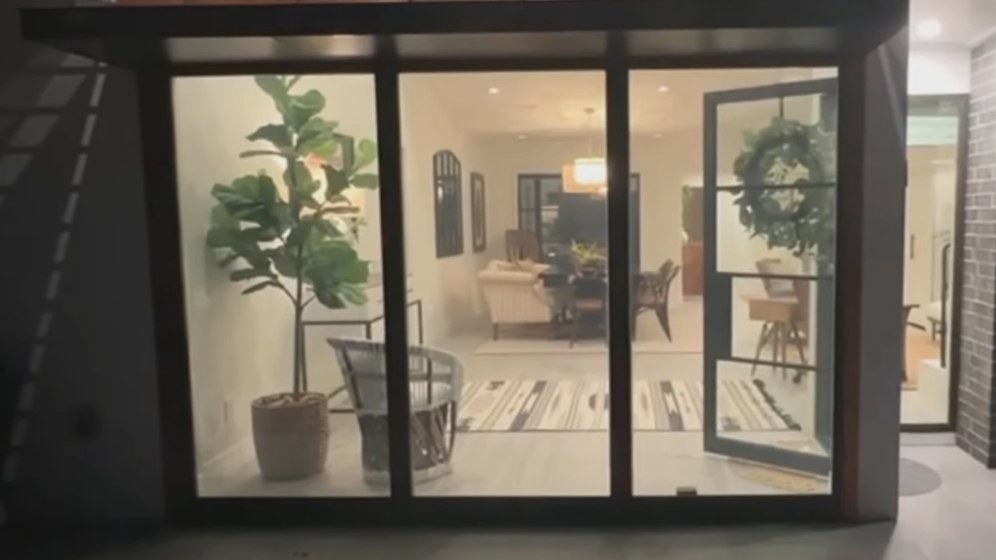 The identical wall from the identical camera position with the power on: the panels are completely clear, showing the plant, the seating and the lit dining room beyond.