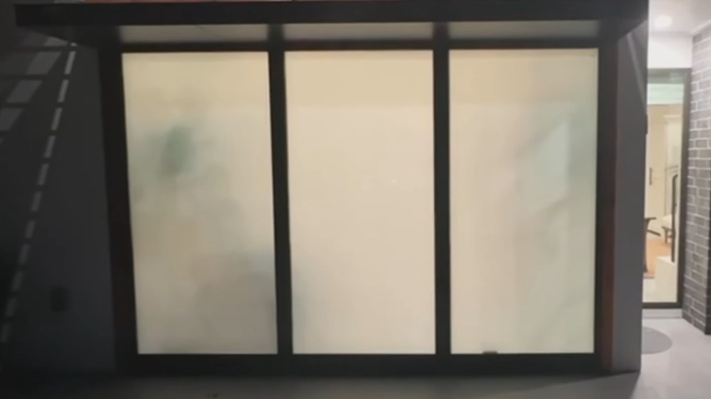A three-panel glass wall between a covered patio and a living room with the power off: every panel is milky white and nothing inside the house can be seen.