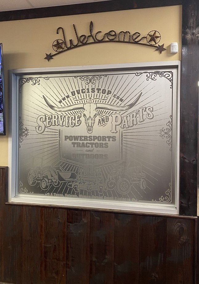 A large etched glass panel showing a detailed illustrated scene, viewed from inside the store.